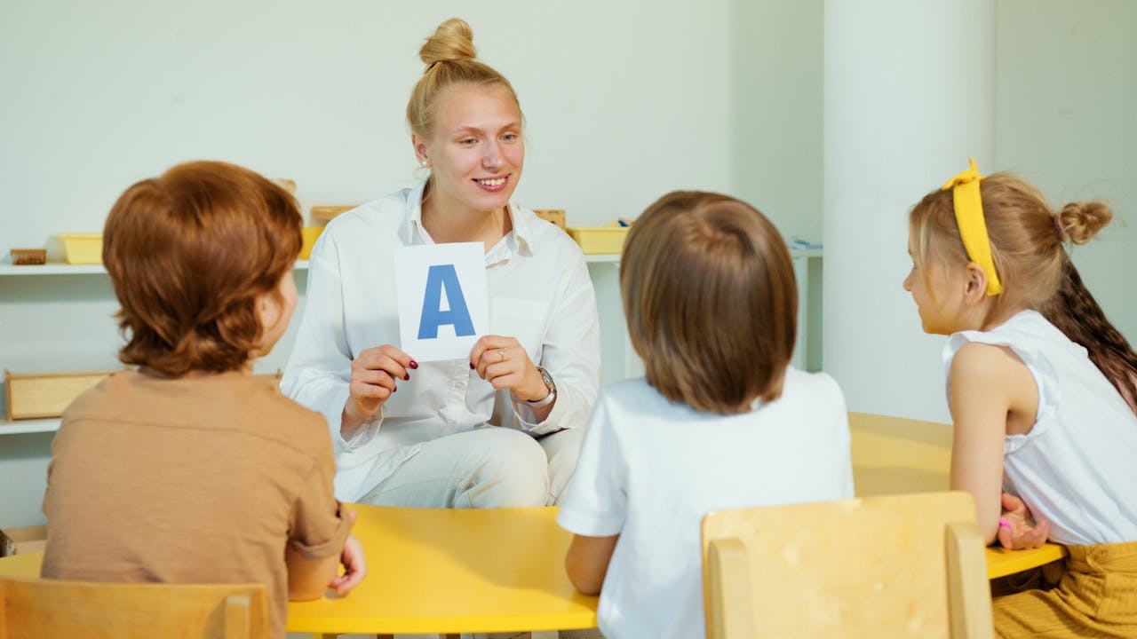 awards-img A teacher holds up a letter card while interacting with preschool children in a classroom setting.